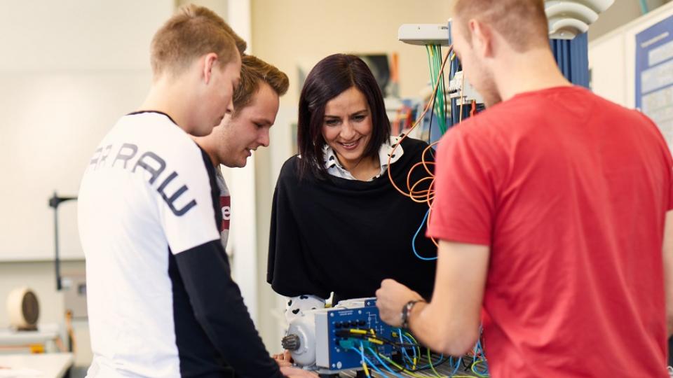 Unterrichtssituation mit 3 jungen Erwachsenen und einer Lehrerin an einer Maschine